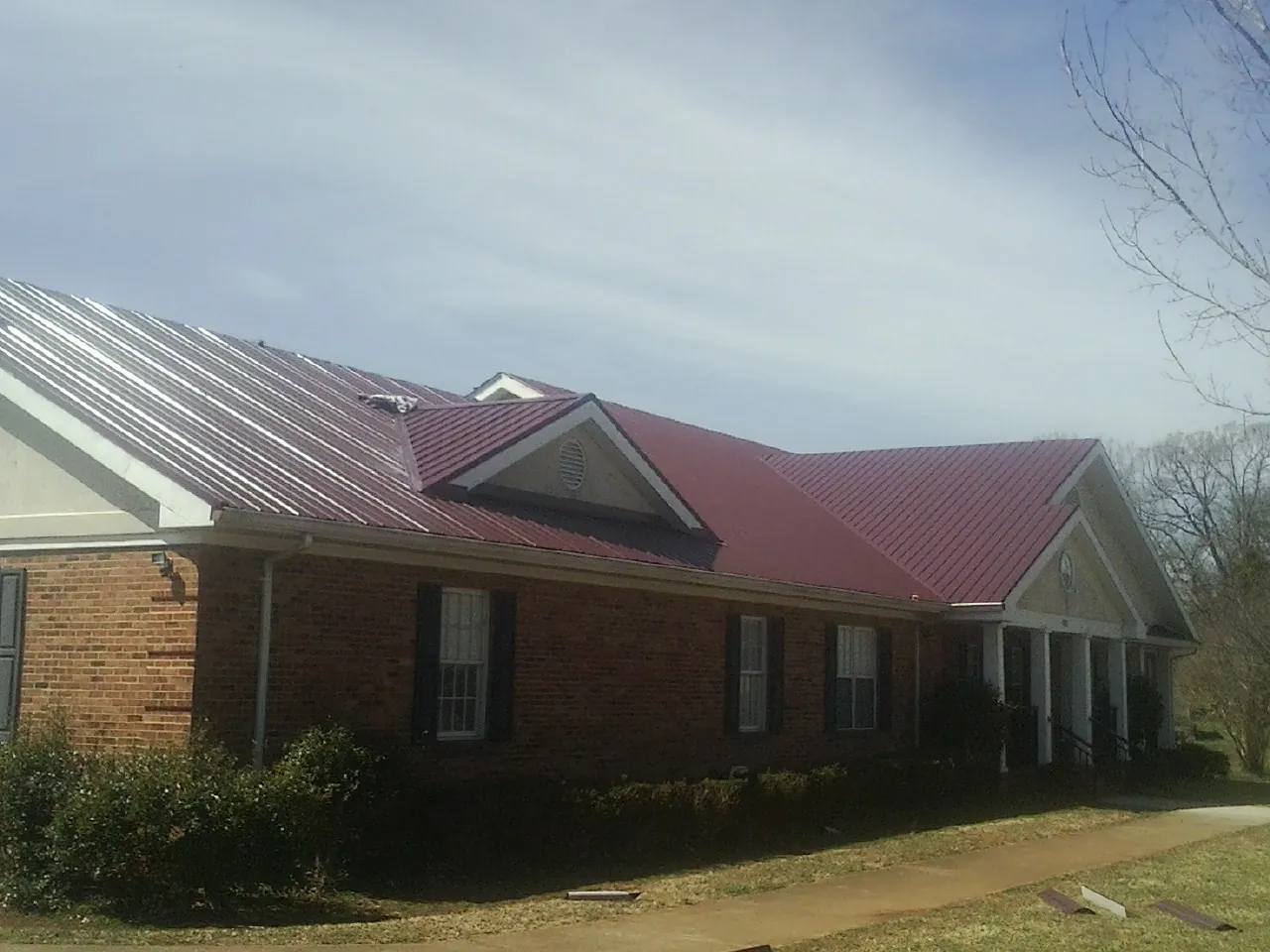 Red metal roof with gabled entries on a long brick building, from a Hail Damage Roof Repair job in Lititz