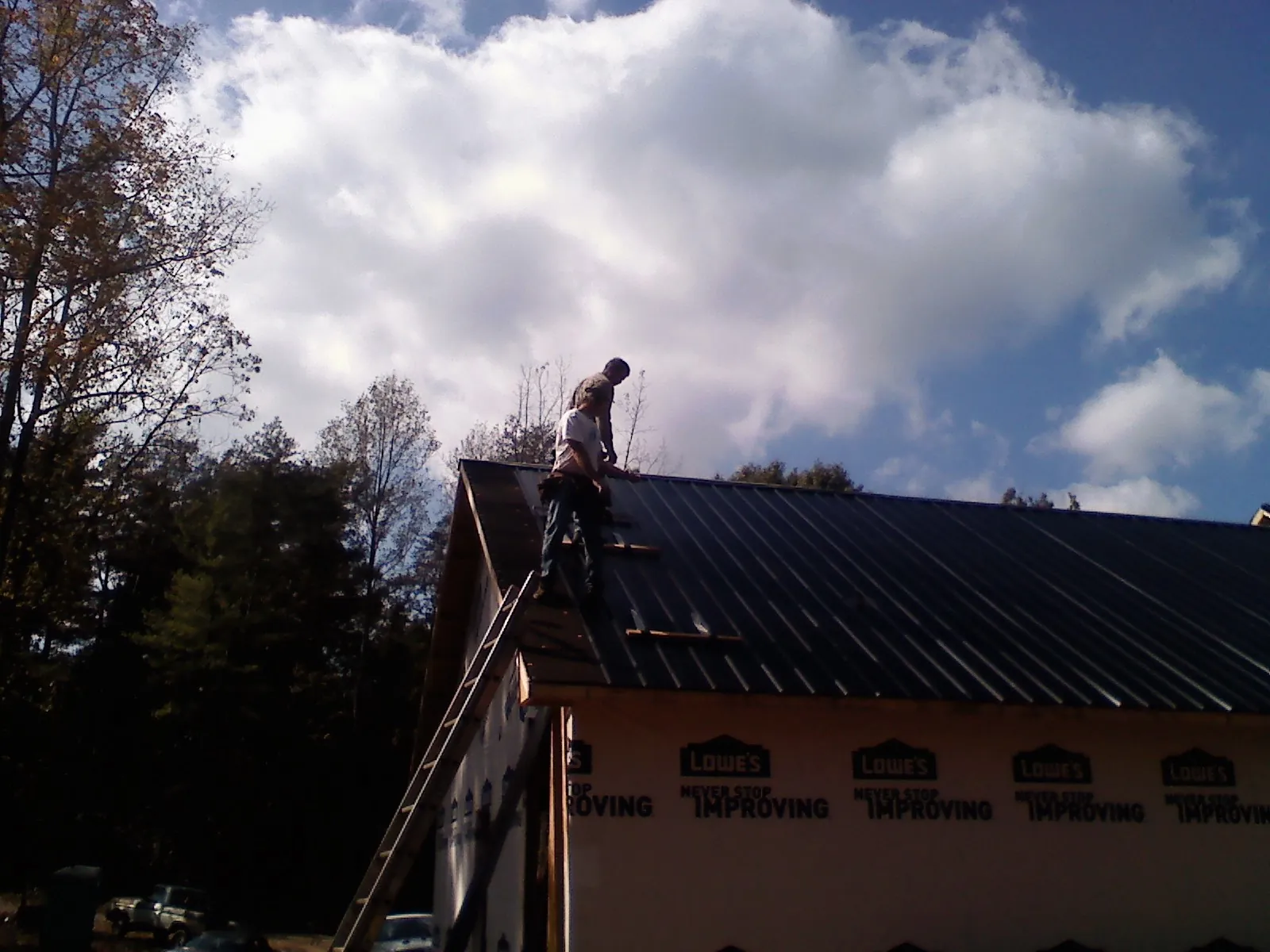 Roofer fastening dark metal panels high against a cloudy sky, from a Roof Inspection job in Lititz