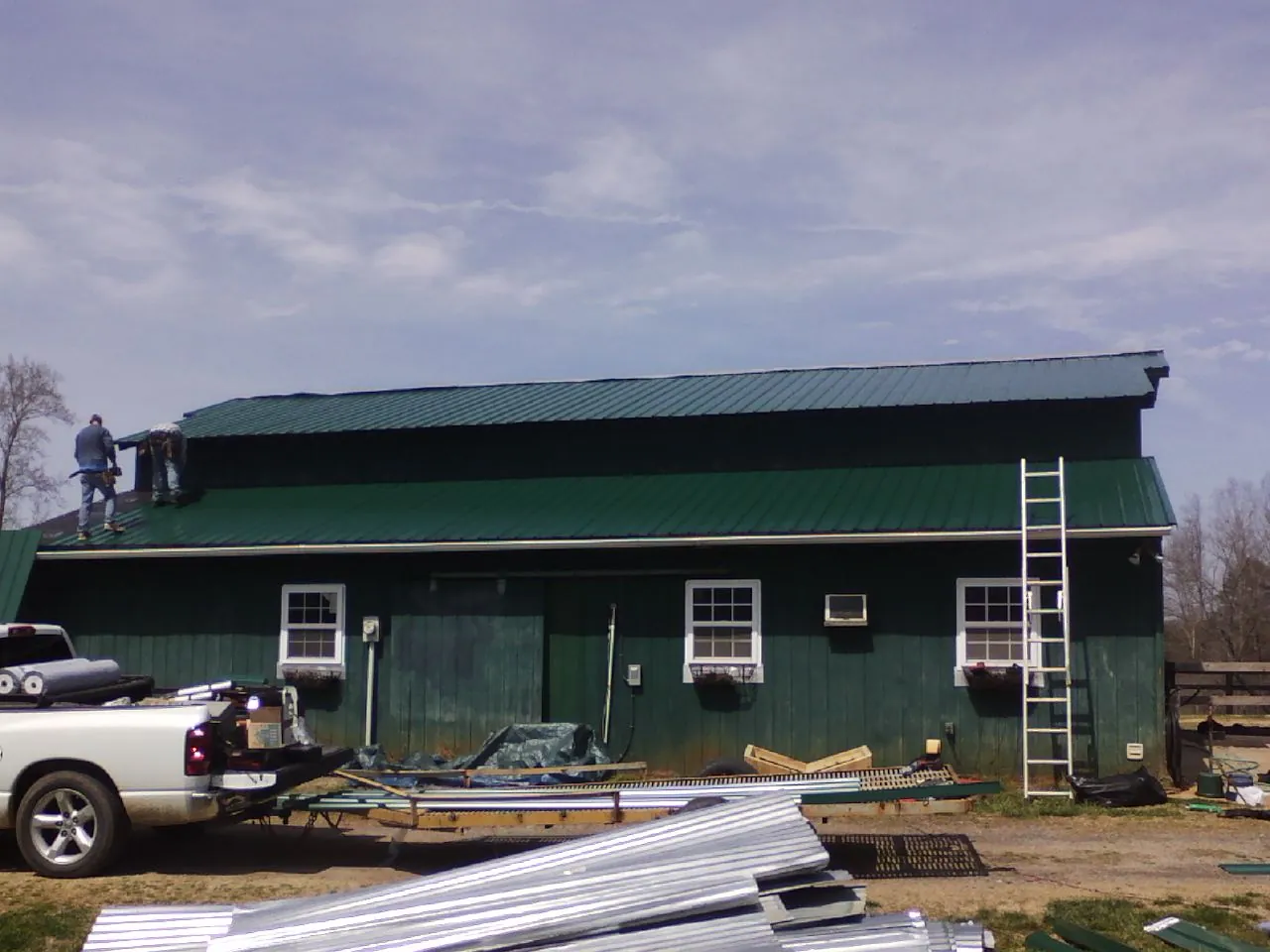Crew installing green metal roofing on a large green barn in Lititz