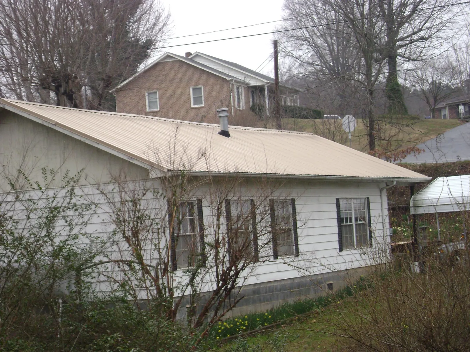 Tan metal roof on a white sided house set into a hillside — Commercial Roofing by Roofing Brothers in Lititz